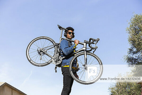 Young man carrying bicycle under clear blue sky