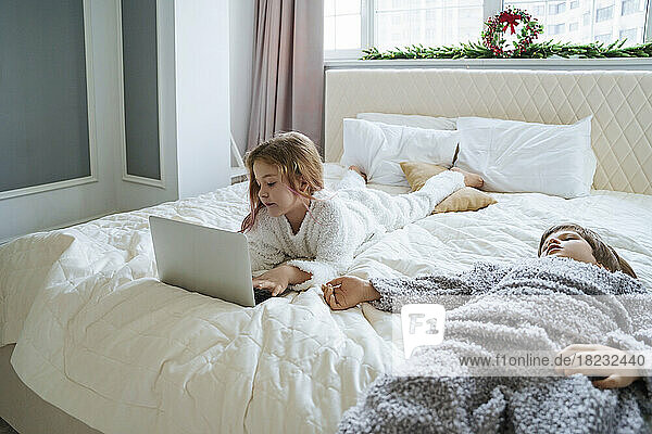 Mädchen benutzt Laptop und liegt zu Hause neben ihrem Bruder im Bett