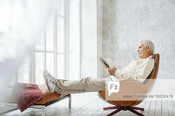 Älterer Mann  der zu Hause auf einem Stuhl sitzt und ein Buch liest