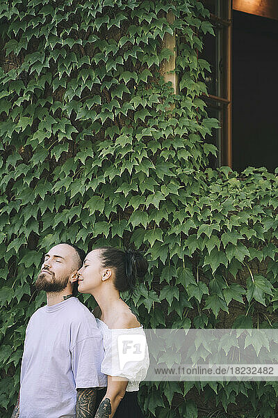 Liebevolles Hipster-Paar steht vor grünen Efeupflanzen