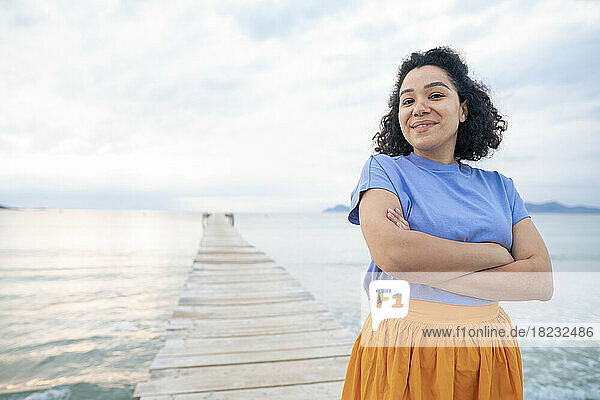 Smiling woman with arms crossed amidst sea