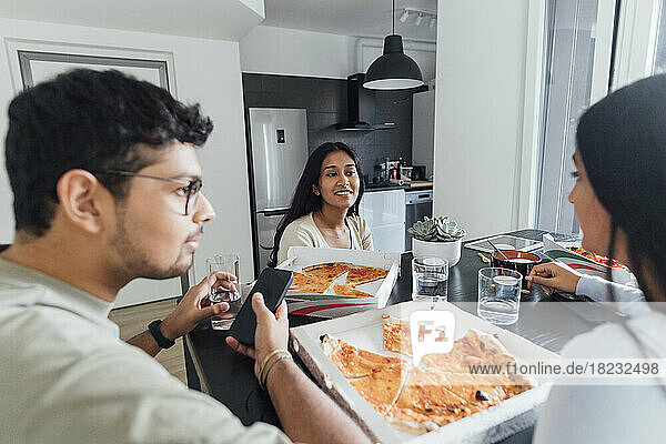 Man holding mobile phone sitting with women and having pizza at home