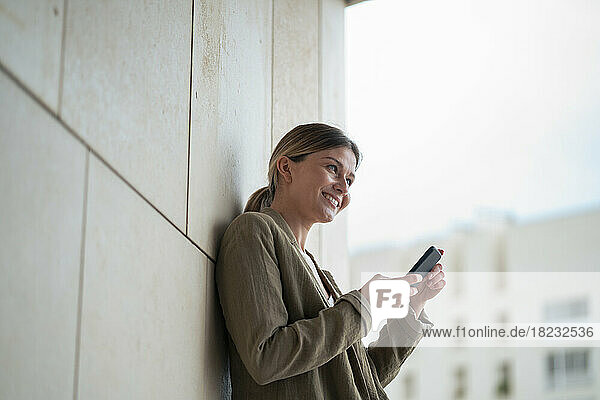 Smiling businesswoman with mobile phone in front of wall