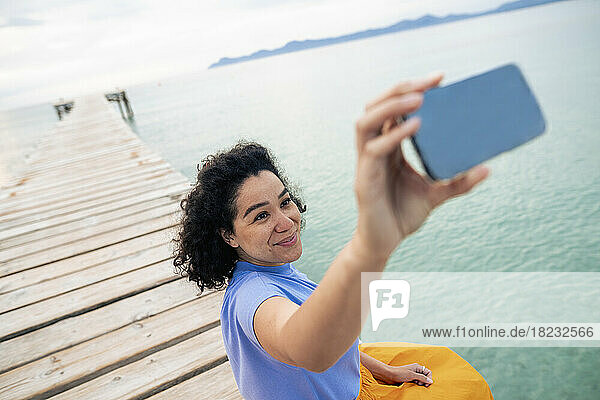 Smiling woman taking selfie through mobile phone on jetty