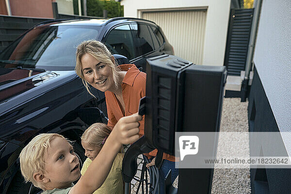 Son paying through credit card by mother holding electric vehicle charger plug in front yard