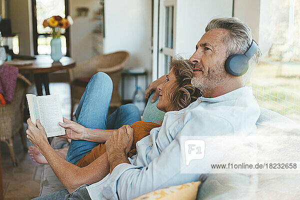 Reifer Mann mit kabellosen Kopfhörern sitzt neben Frau mit Buch