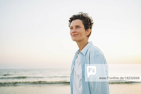 Thoughtful androgynous woman standing at beach