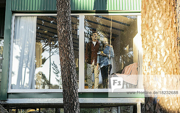 Älteres Paar steht am Fenster eines Hauses und schaut hinaus