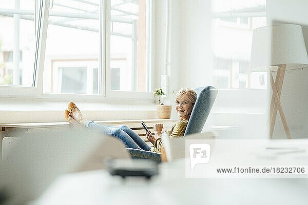 Smiling businesswoman with smart phone on armchair at office