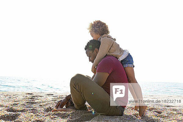 Girl embracing father sitting at beach on sunny day