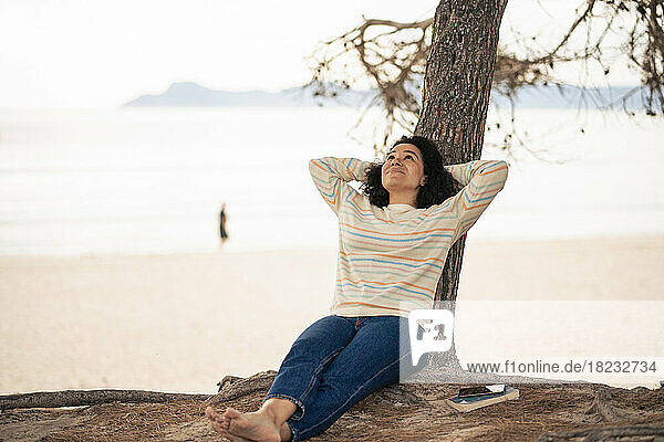 Woman with hands behind head relaxing by tree