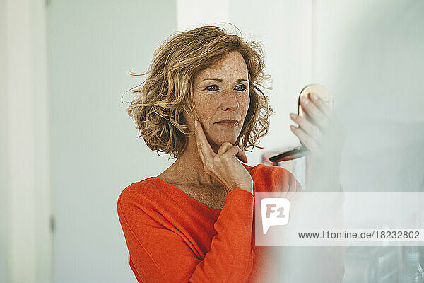 Smiling mature woman looking in mirror at home