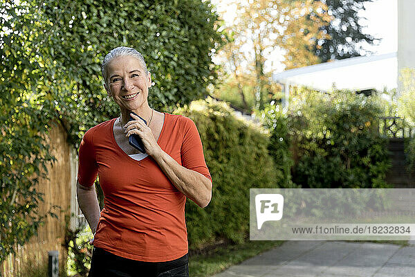 Smiling senior woman wearing orange t-shirt holding mobile phone in garden