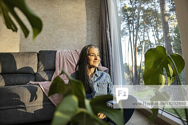 Smiling mature woman looking out of window at home