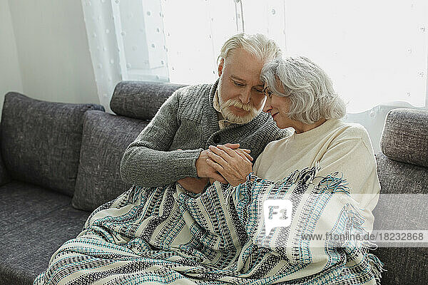Senior couple cuddling on the couch under a blanket