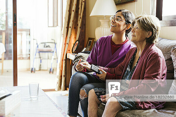 Happy senior woman watching TV with caregiver at home