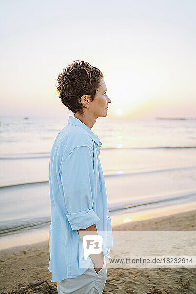 Nachdenkliche Frau steht bei Sonnenuntergang am Strand