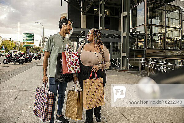 Happy young couple standing with shopping bags on footpath