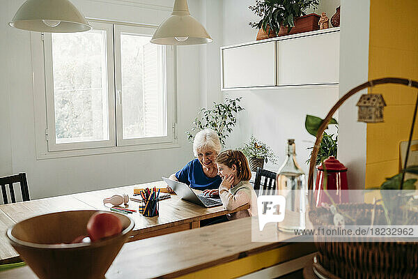 Ältere Frau hilft Enkelin beim Lernen per Laptop auf dem heimischen Tisch