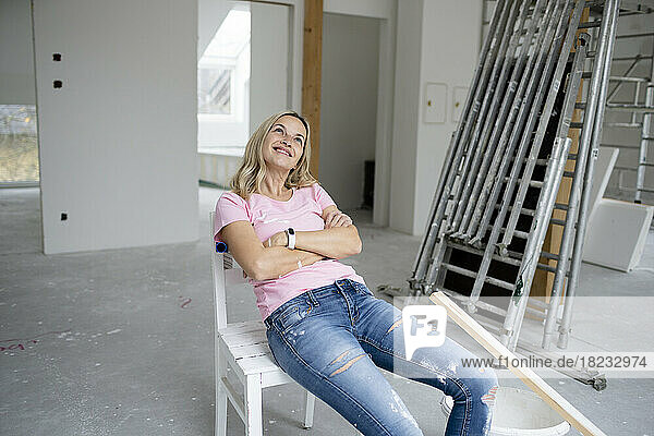 Smiling woman day dreaming sitting on chair with arms crossed in apartment
