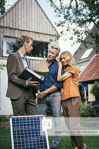 Real estate agent having discussion with customers standing in front of house