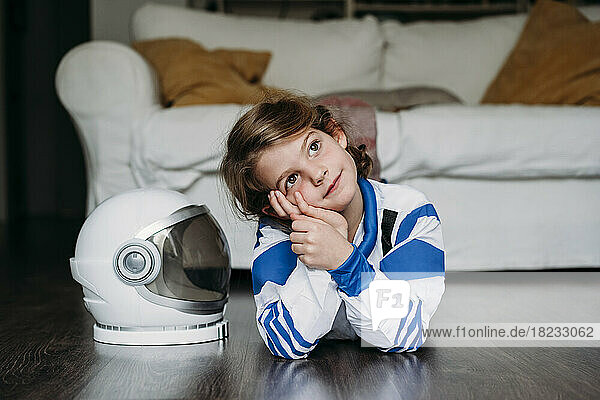 Nachdenklich lächelndes Mädchen im Weltraumkostüm  das zu Hause neben dem Helm auf dem Boden liegt