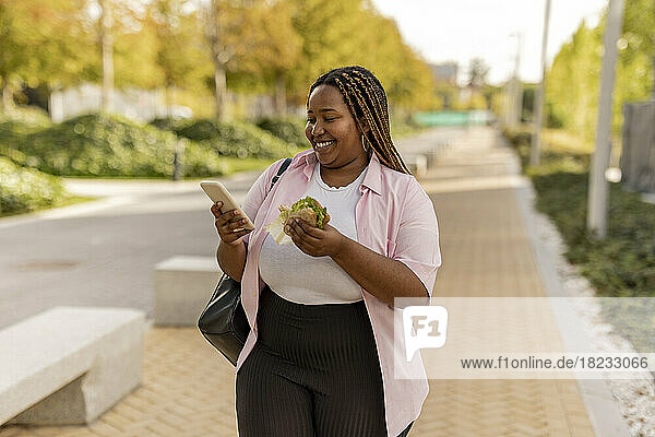 Glückliche junge Frau benutzt Smartphone am Fußweg