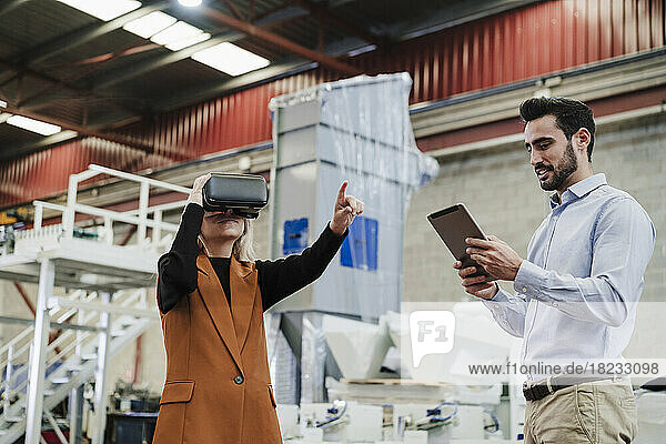 Businessman using tablet PC with colleague gesturing by wearing virtual reality simulator