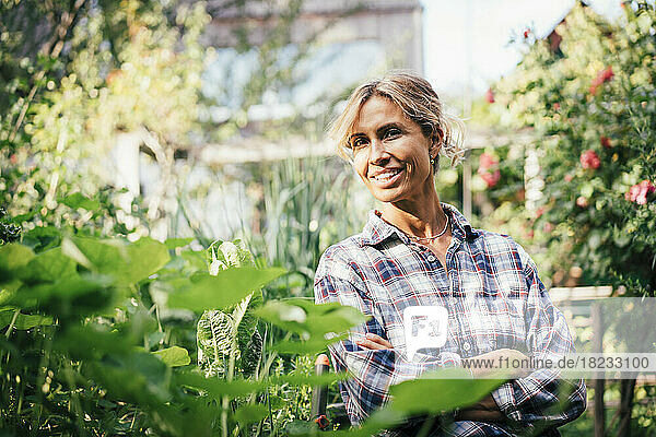 Mature woman smiling with arms crossed in vegetable garden