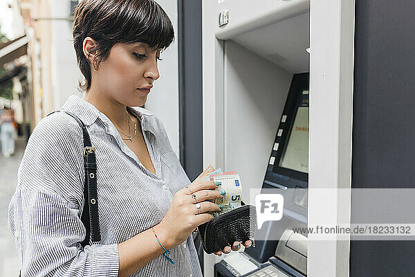 Young woman counting money from purse at ATM machine