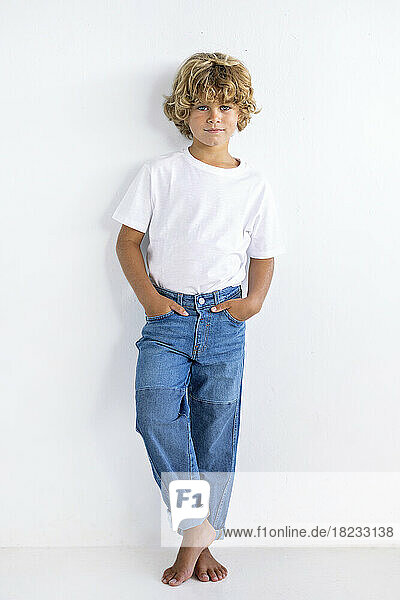 Boy with hands in pockets standing against white background