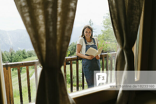 Happy young woman with book seen through window