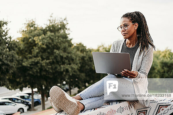 Thoughtful mature woman sitting with laptop on terrace at sunset