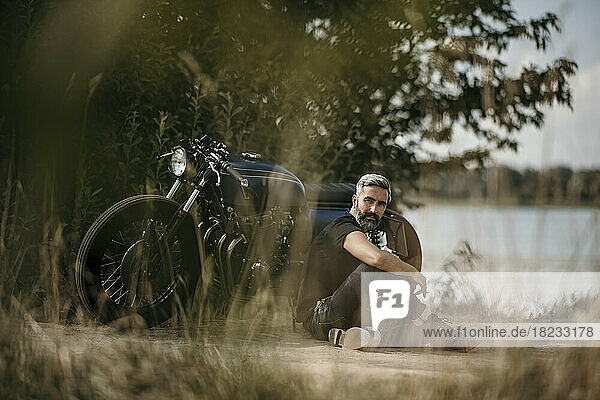 Thoughtful mature man sitting in front of motorcycle