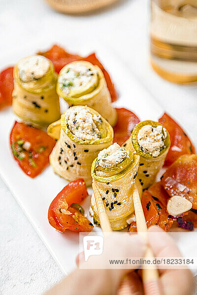 Personal perspective of woman eating zucchini and ricotta rolls with tomato salad