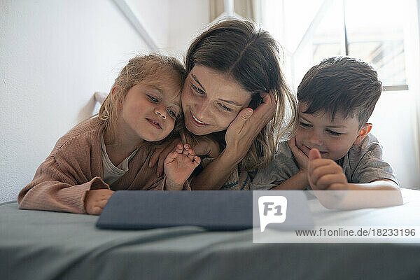 Lächelnde junge Frau mit Kindern nutzt Tablet-PC im heimischen Schlafzimmer