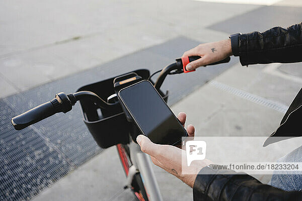 Hand of man renting bicycle through mobile phone on footpath