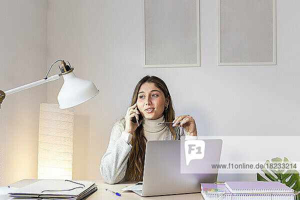 Young woman talking on smart phone at desk