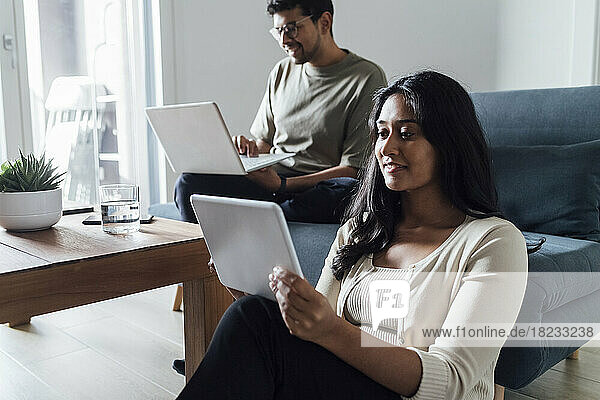 Junge Frau lernt zu Hause über Tablet-PC mit Mann im Hintergrund