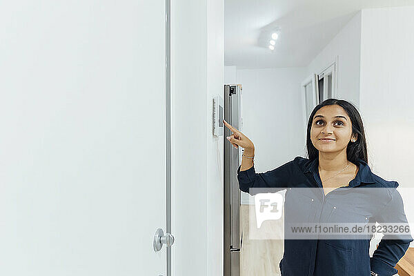 Smiling young woman using smart home device on wall