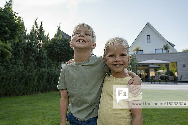 Happy girl with arm around brother in garden