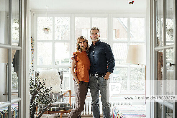 Smiling man and woman standing with hands in pockets at home
