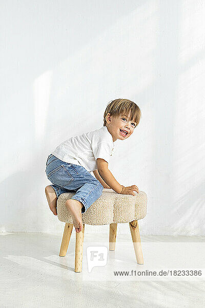 Boy playing on stool in front of wall at home