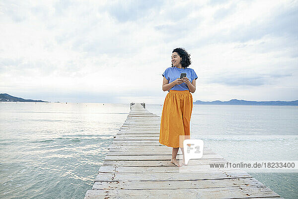 Smiling woman standing with smart phone on jetty