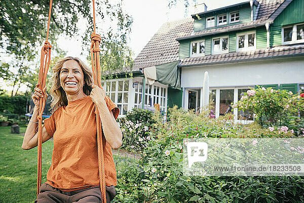 Cheerful mature woman sitting on swing in front of house