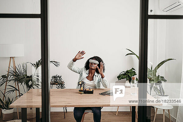 Freelancer wearing virtual reality headset with robotic model on desk at home