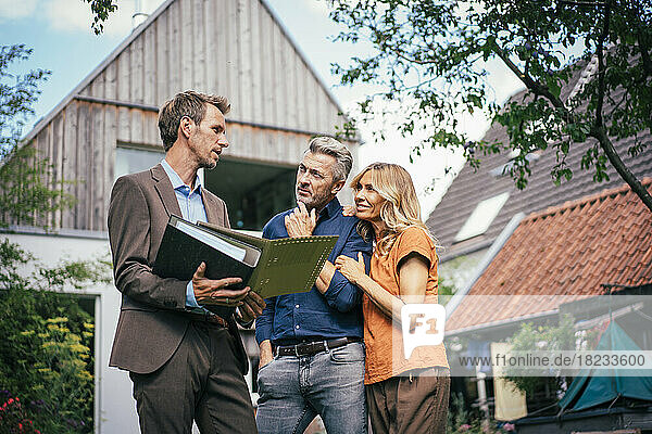 Mature couple discussing over documents with real estate agent in front of house