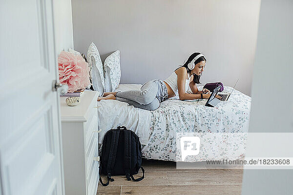 Girl with headphones lying on bed using wireless technologies at home