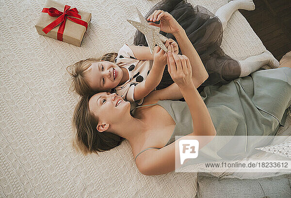 Happy mother and daughter playing with Christmas star on bed at home
