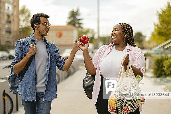 Smiling man with woman holding bag of vegetables walking on footpath